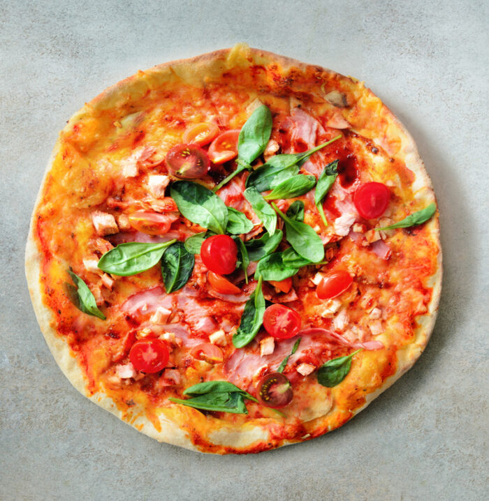 Pizza congelada llesta per servir amb trossos de bacó, tomàquet i fulles d'alfàbrega.